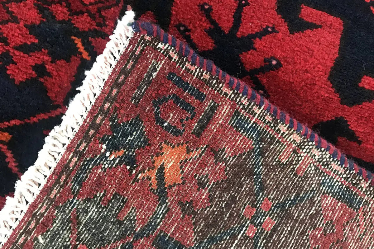 Edge and fringe of a red and dark blue runner rug with a fine line pattern.