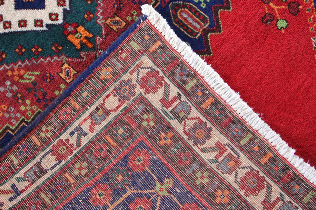 Detail of the carpet edge: red fabric with a blue pattern, white trim, and fringes