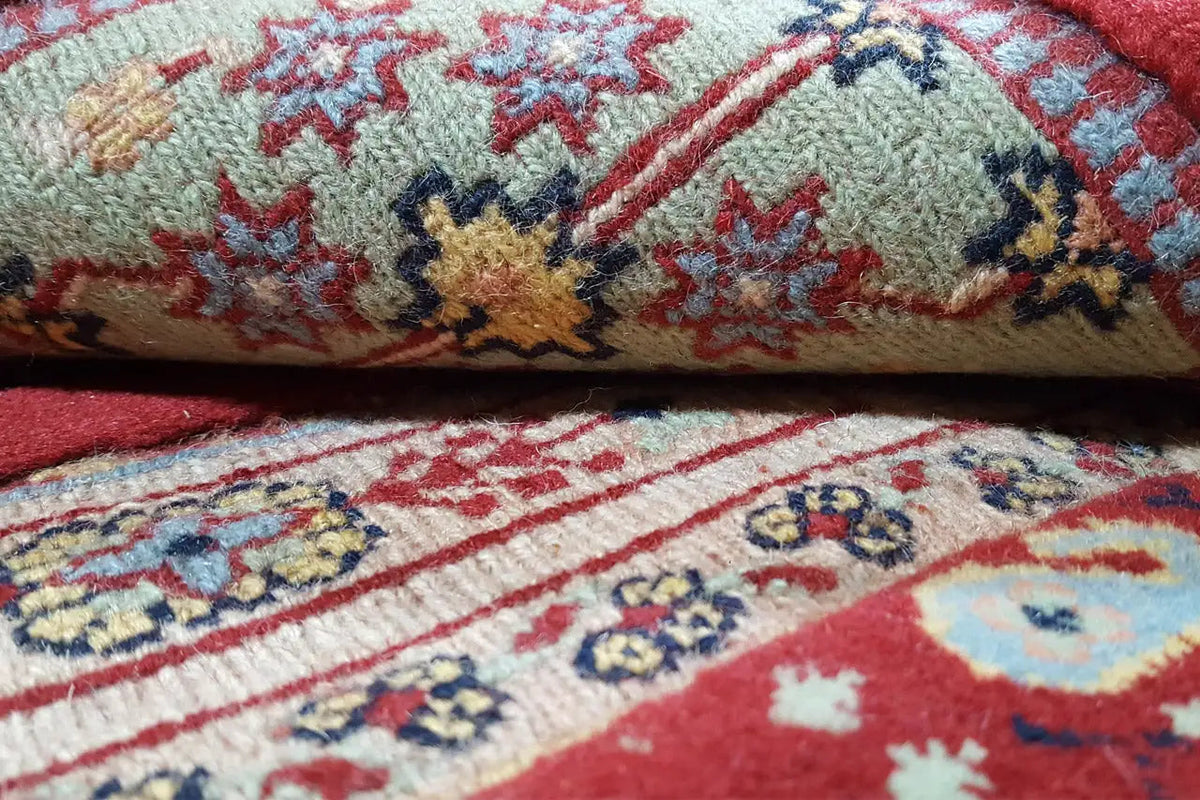 Carpet detail: knotted pile with a red, blue, and beige ornamental pattern near the edge