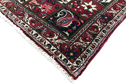 Corner view of an oriental rug with fringes and a border in red, dark blue, and cream