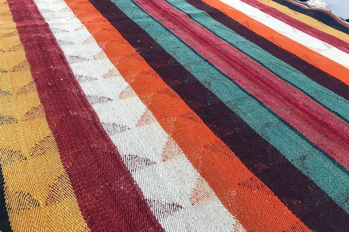 Close-up view of Jajim rug: dense texture with a striped pattern in orange, green, and blue