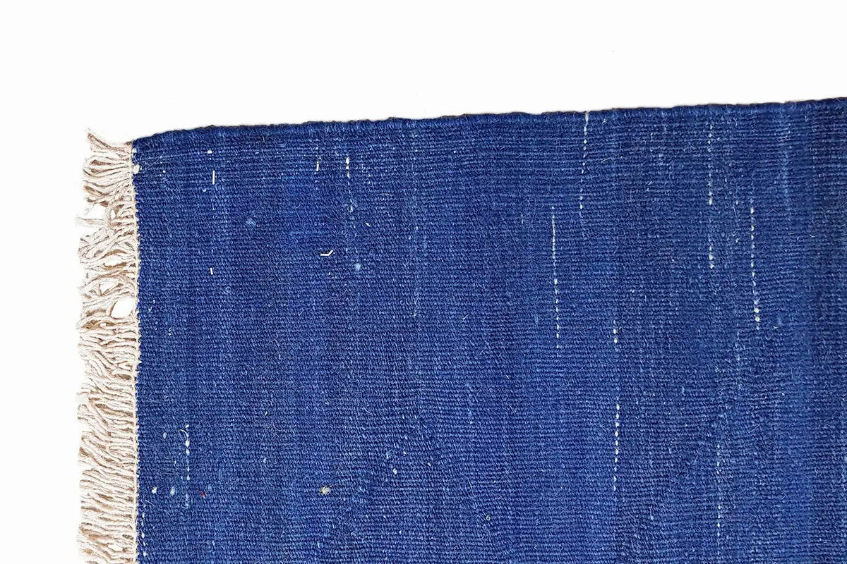 Blue kilim rug, fringe along the side edge, light lines in the weave