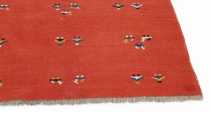 Red kilim rug with small multicolored patterns and fringe along the edge