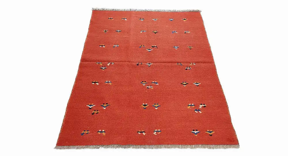 Red kilim rug at an oblique angle with multicolored geometric motifs and fringes