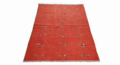 Red kilim rug at an oblique angle with multicolored geometric motifs and fringes