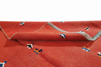 Red kilim rug with woven-in patterns, visible edge with fringes