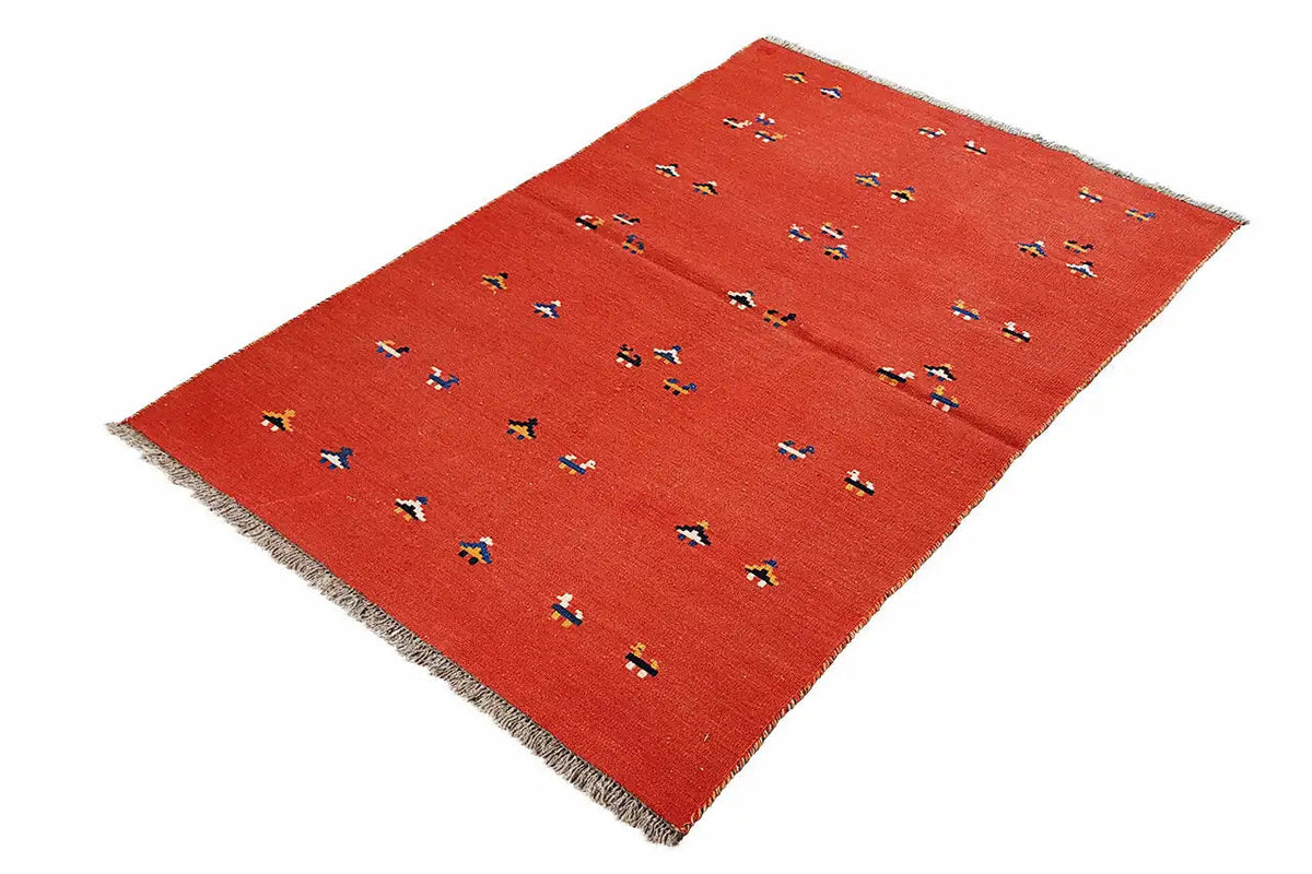 Red kilim rug at an angle with colorful geometric patterns and fringes
