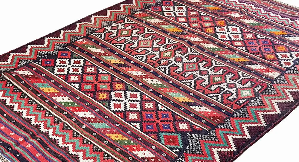 Close-up of a kilim rug: geometric ornaments and stripes in red, blue, green, and black.