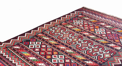 Kilim rug close-up: diagonal stripes and diamond patterns in red, blue, white, and green.