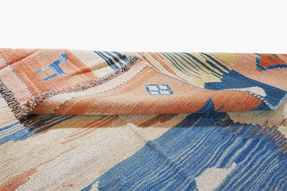 Kilim rug detail with fringe and a geometric pattern in blue, orange, and cream