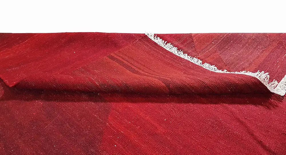 Red kilim rug with a fine patterned weave and short white fringes along the edge