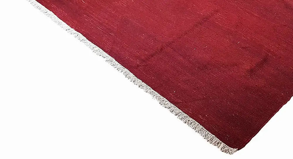 Red kilim rug in triangular view with white edging fringes and a smooth woven texture