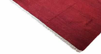 Red kilim rug in triangular view with white edging fringes and a smooth woven texture