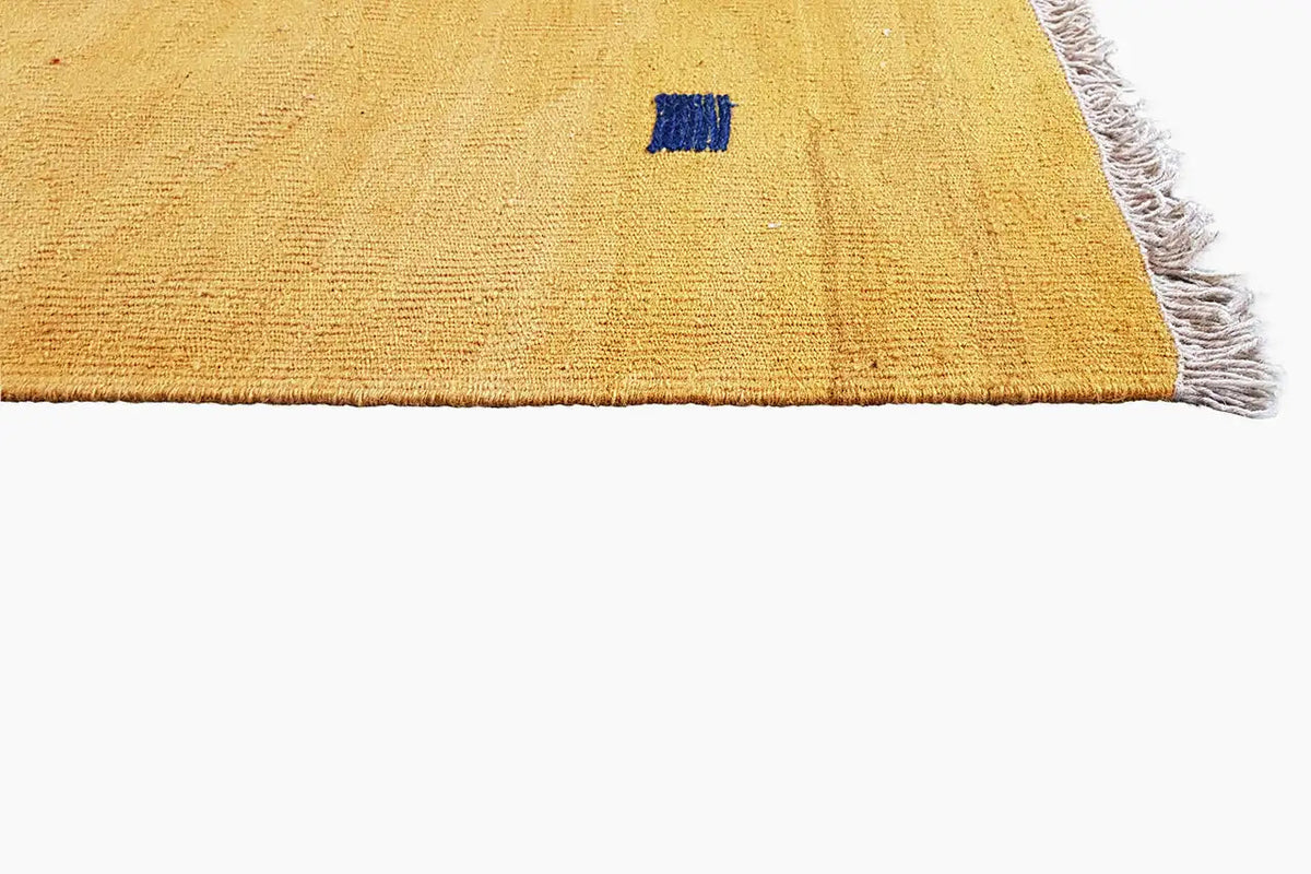Corner section of an ochre kilim rug with a blue square and fringes