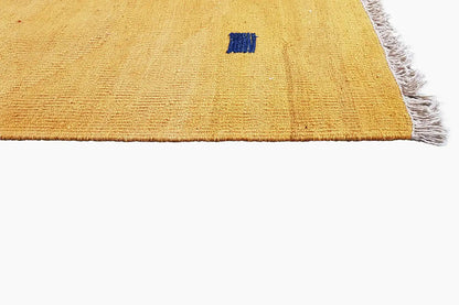 Corner section of an ochre kilim rug with a blue square and fringes