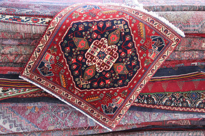 Qashqai rug by Poschti: red rug laid diagonally with a medallion and fringes.