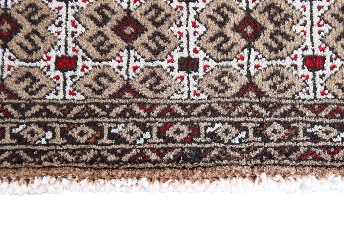 Detail of a Turkmen carpet: rows with diamond patterns and a decorative border, fringes along the bottom edge