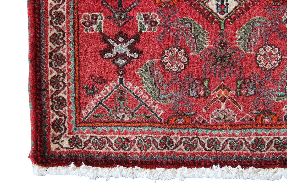 Corner view of a red carpet with a multicolored border and fringe