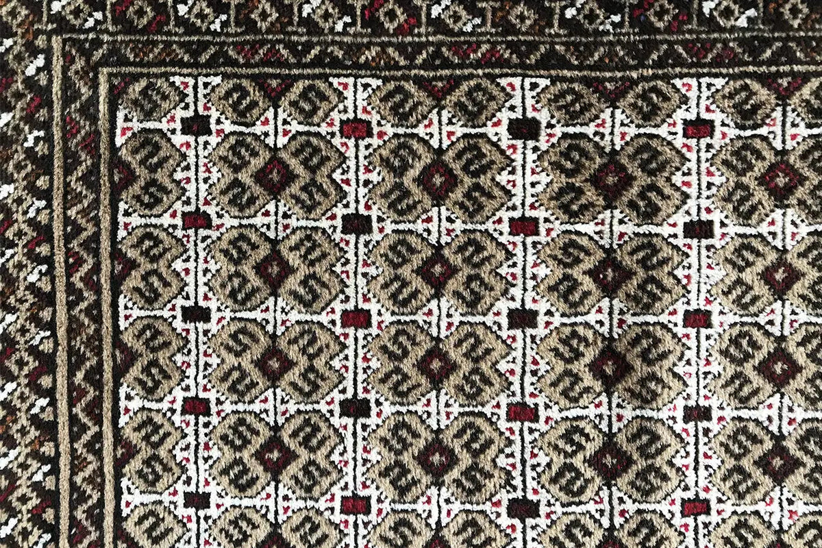 Turkmen carpet detail view: rectangular field with rows of ornaments in beige and dark brown