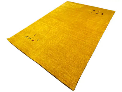 Yellow Gabbeh rug, lying at an angle, with delicate animal and plant motifs across its surface