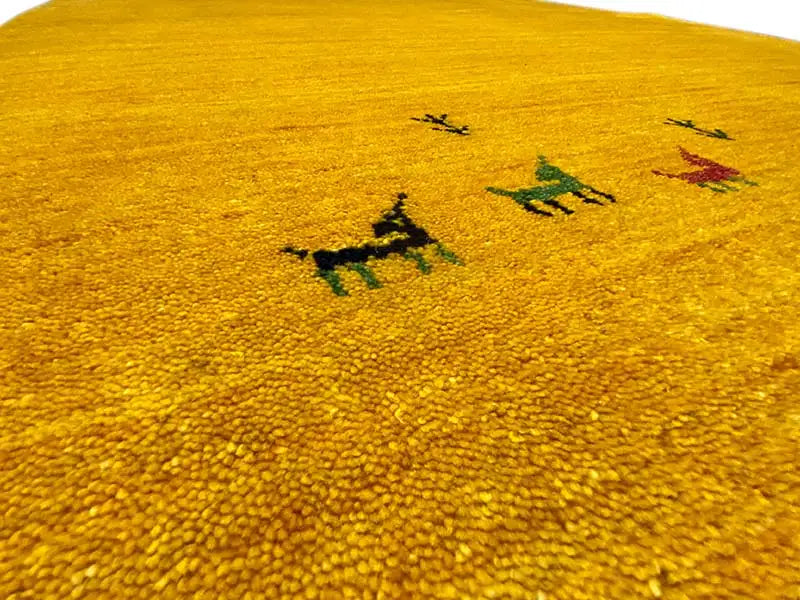 Close-up: yellow Gabbeh rug with a dense pile and colorful animal motifs