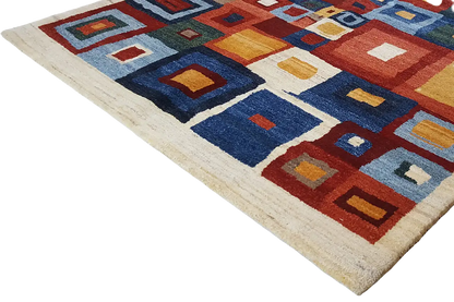 Corner view of a Gabbeh rug with geometric squares in blue, red, and beige