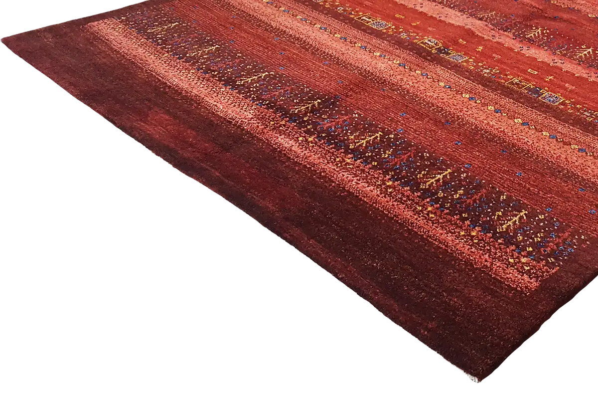 Gabbeh rug in reddish brown with a striped pattern and colorful accents, shown at an angle.