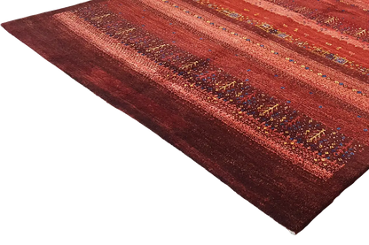 Gabbeh rug in reddish brown with a striped pattern and colorful accents, shown at an angle.