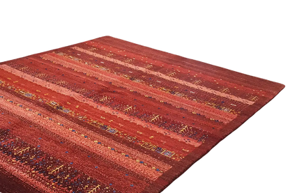 Gabbeh rug: wide reddish-brown stripes with fine dots and multicolored accents.